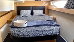 A compact bed with patterned bedding, a bedside table, and a window with curtains.