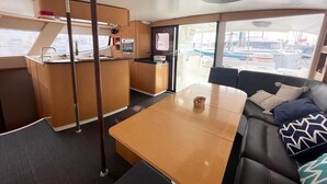 A modern interior with a wooden table, a sofa with patterned cushions, a kitchen area, and a view of the marina through large windows.
