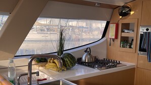 A compact kitchen with a stainless steel sink, a gas stove, and a window offering a view of a marina.