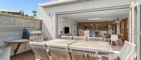 Une terrasse extérieure avec des meubles en bois, un barbecue et une vue sur une cuisine moderne.