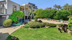 Una casa moderna de dos pisos con un jardín bien cuidado, que incluye arbustos variados y césped.