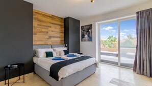 Un dormitorio moderno con una cama grande, una mesita auxiliar pequeña, un muro de acento de madera, un ventanal con vistas y una lámpara en el techo.