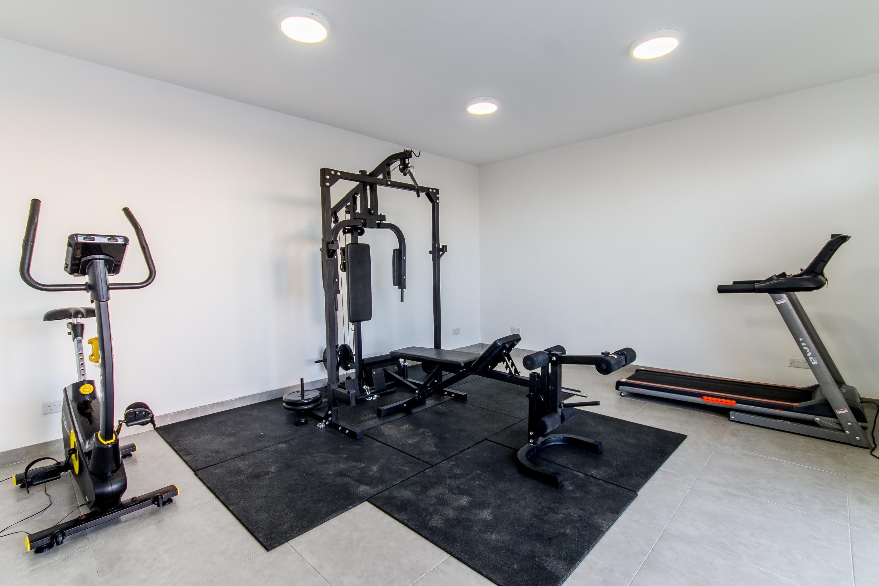 A gym with a stationary bike, weight bench, and a treadmill.