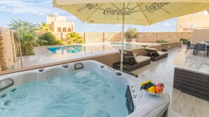 Un jacuzzi con un paraguas de Coca-Cola, una piscina, mobiliario exterior y vistas a un edificio histórico.