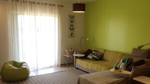 A living room with a green wall, a sofa, a bean bag, a small table, and a lamp. - Magnificent 2 bedroom ground floor apartment, wi-fi, pool, garden, near beach and golf - Galé, Albufeira (Albufeira)