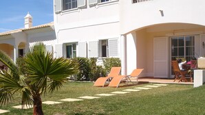 A white building with a covered patio area, two orange lounge chairs, and a palm tree. - Magnificent 2 bedroom ground floor apartment, wi-fi, pool, garden, near beach and golf - Galé, Albufeira (Albufeira)