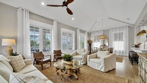 Ein geräumiges Wohnzimmer mit einem Glastisch, weißen Sofas und einem Deckenventilator.