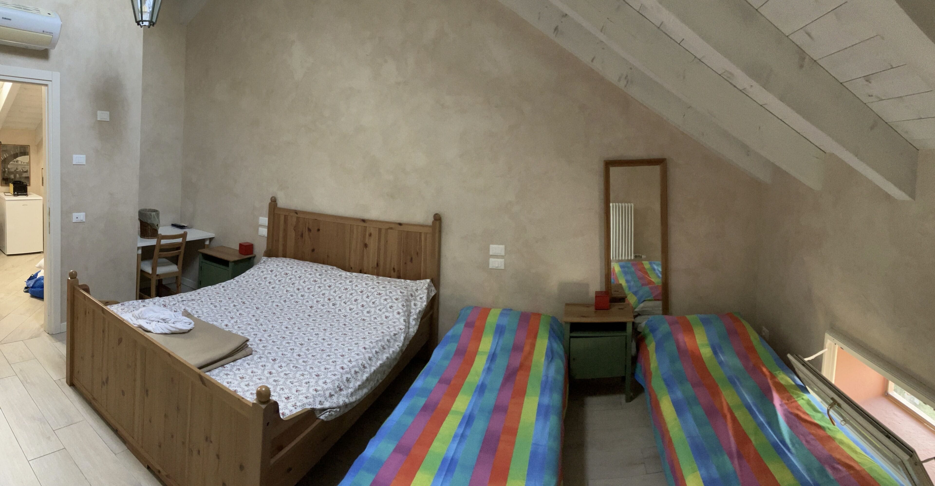 A bedroom with a wooden bed, a small desk, a chair, and a colorful striped bedspread.