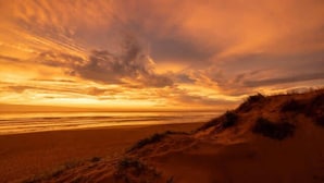 Une plage avec des dunes et un ciel au coucher du soleil.