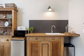 A kitchen with wooden cabinets, a microwave, a sink, and a small refrigerator. - The Ancient Mariner Retreat (Cape Woolamai)