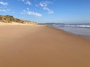 A wide sandy beach with gentle waves, a clear sky, and distant hills. - The Ancient Mariner Retreat (Cape Woolamai)