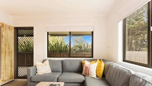 Een moderne woonkamer met een grijze bank, een houten salontafel en een groot raam met uitzicht op groen.