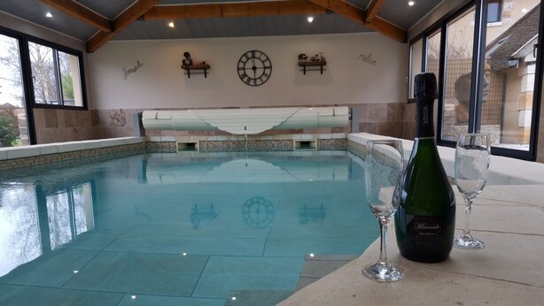 Una piscina interior con vista despejada al techo y a las paredes, una botella de vino y un vaso junto a la piscina.