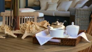 Ein Zimmer mit einem Holzbstuhl, einem Korbsessel und einem kleinen Tisch mit Teekanne und Tassen.