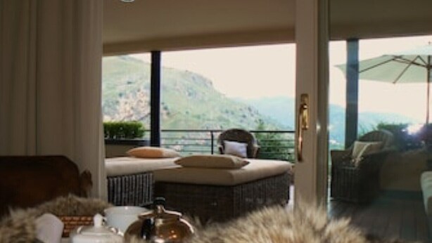 Ein gemütliches Zimmer mit einem mit Fell überzogenen Bereich, einer Couch und Blick auf eine gebirgige Landschaft durch eine Glastür.