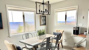 Un espace repas comprenant une table, des chaises, une machine à café et une vue sur l’extérieur.
