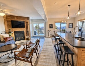 A modern kitchen with a bar area, a fireplace, and a large window offering a view of the outdoors.
