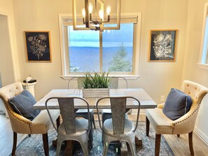 Uma sala de jantar com mesa e cadeiras, um lustre e duas obras de arte com flores emolduradas nas paredes.