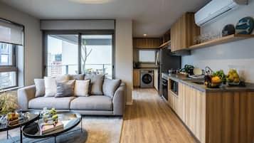 Un apartamento moderno con un sofá gris, una mesa de comedor, una cocina con armarios de madera y una lavadora integrada.