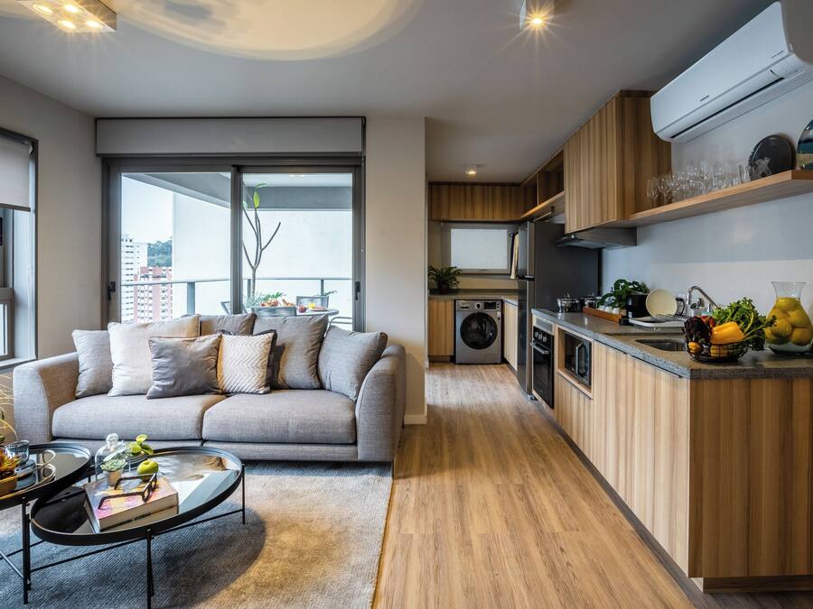 Un apartamento moderno con un sofá gris, una mesa de comedor, una cocina con armarios de madera y una lavadora integrada.