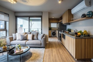 Un apartamento moderno con un sofá gris, una mesa de comedor, una cocina con armarios de madera y una lavadora integrada.