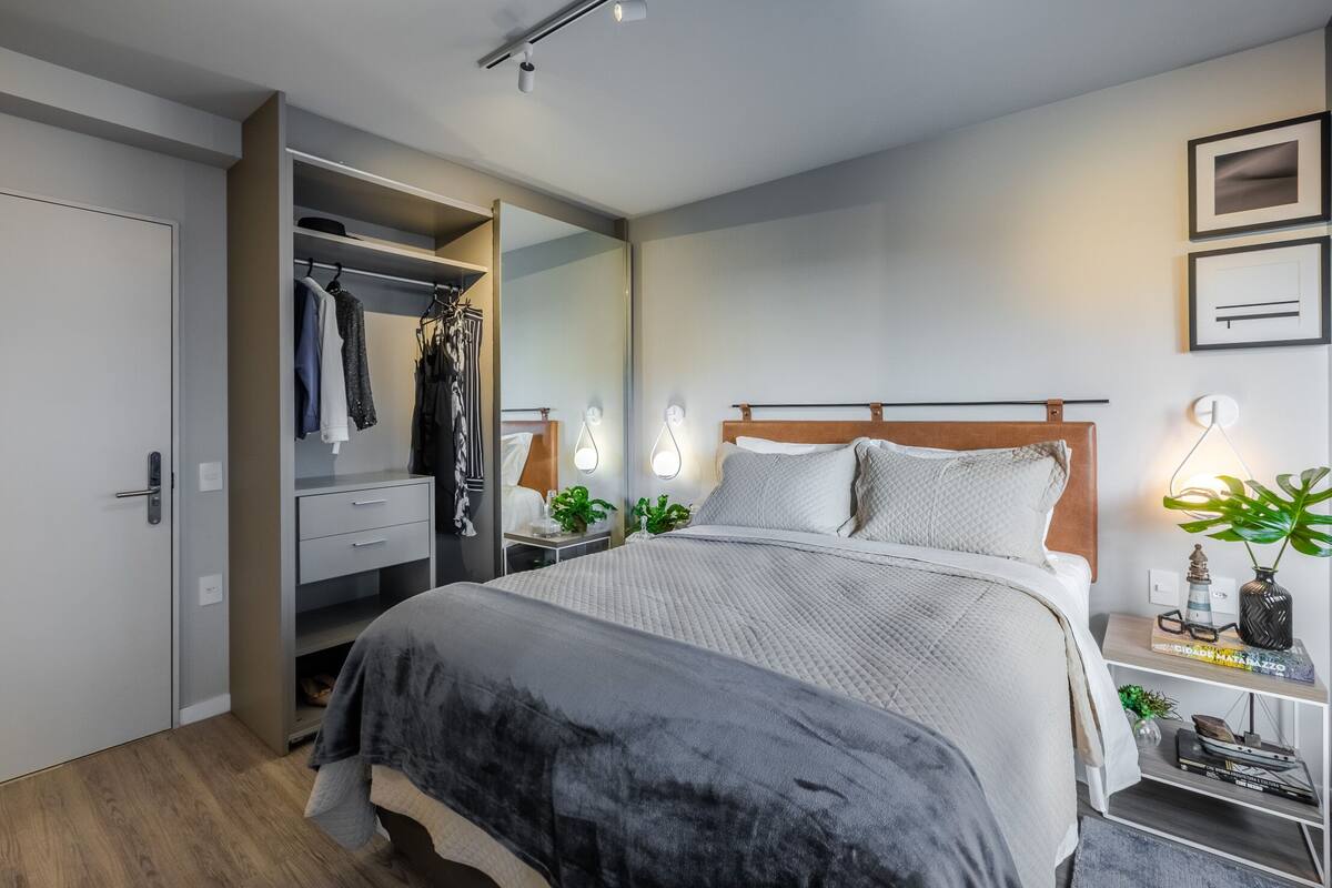 Un dormitorio moderno con una cama grande, un vestidor, lámparas de noche y una mesita de noche con una planta.