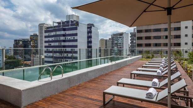 Zona de piscina en la azotea con sillones de descanso y una barandilla de cristal.
