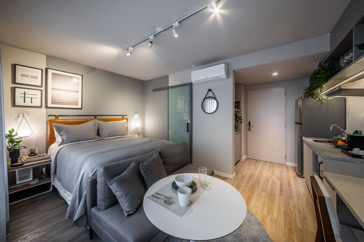 Un dormitorio moderno con cama, mesita de noche y una mesa redonda con un cuenco y una taza.