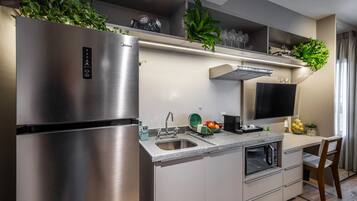 A modern kitchen with a stainless steel refrigerator, a built-in oven, and a microwave. There is a sink with a faucet, a countertop with a bowl of fruit, and a chair.