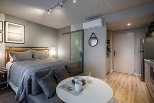 Un dormitorio moderno con cama, mesita de noche y una mesa redonda de comedor con un tazón y una taza.
