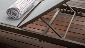 A row of sun loungers with towels, wooden flooring, and a modern building in the background.