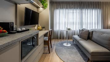 Una cocina moderna con horno integrado, una zona de comedor con mesa redonda y una sala de estar con sofá y televisor.
