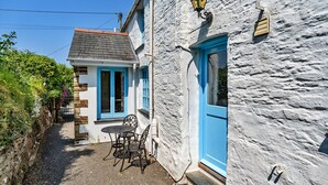 A narrow alleyway with a white building featuring a blue door and window frames. - Forge Cottage (Padstow)