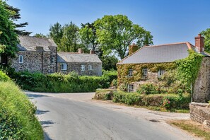 Een smalle weg langs stenen huizen met muur ommuurd met klimop, onder een helderblauwe lucht.