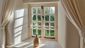 A room with a large window, a vase on a ledge, and curtains. - Forge Cottage (Padstow)