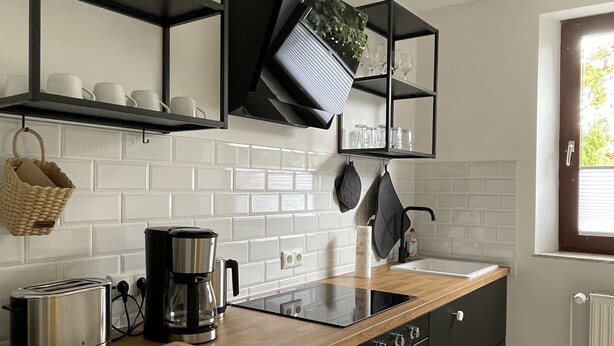 A modern kitchen with black cabinets, a wooden countertop, and a built-in stove. There are shelves above the counter holding glasses and a basket. - Ole School apartment in Jork in the middle of the Altes Land (Jork)