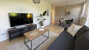 A living room with a flat-screen TV, a sofa, a coffee table, and a dining area with chairs and a table. - Ole School apartment in Jork in the middle of the Altes Land (Jork)