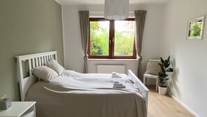 A neatly made bed with white linens, a bedside table with a lamp, a potted plant, and a window with curtains. - Ole School apartment in Jork in the middle of the Altes Land (Jork)