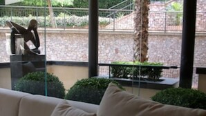 En balkon med sofa, statue og en stenvæg med grønne planter.