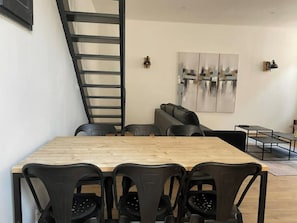A modern dining area with a wooden table and black chairs, a black staircase, a black sofa, and abstract wall art.