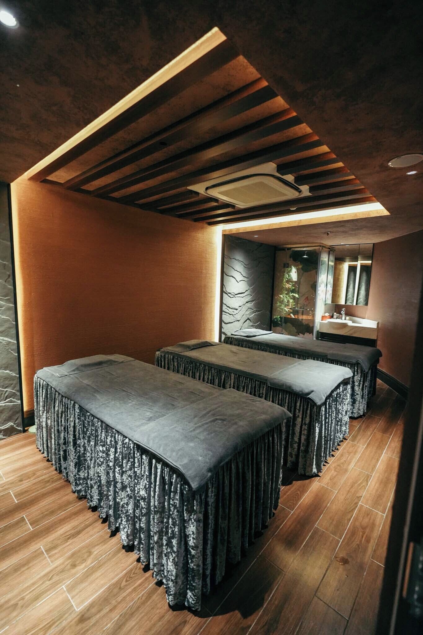 A spa room with two massage tables, a wooden ceiling, and a stone wall.