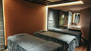 A spa room with two massage tables, a wooden ceiling, and a stone wall.