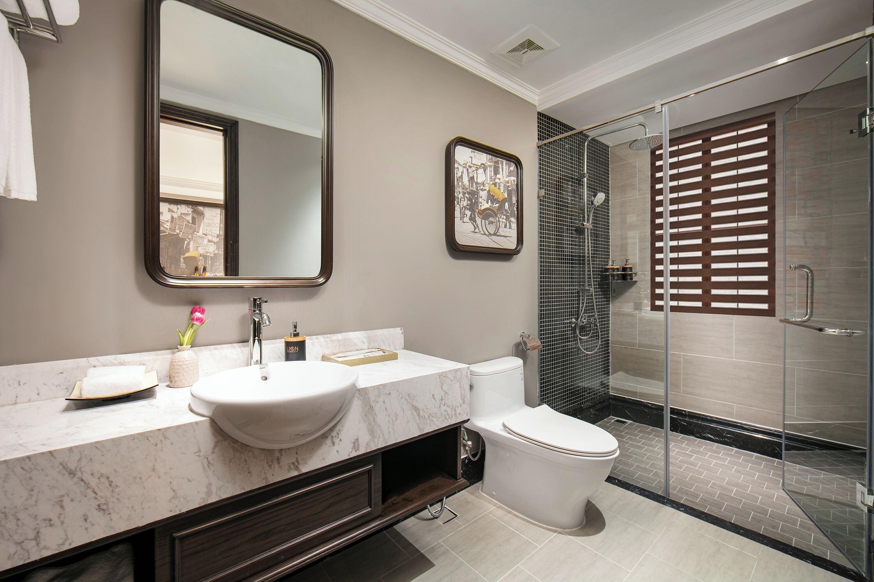 A modern bathroom with a marble sink, a toilet, a large mirror, and a glass shower enclosure.