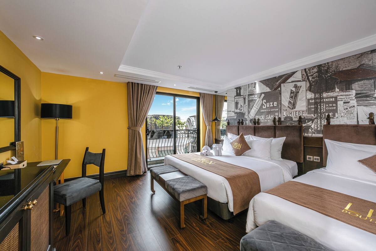 Habitación de hotel con dos camas, un escritorio, una silla y un amplio ventanal con vistas.