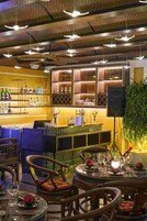 A bar area with shelves of bottles and glasses, a bar counter, and a television. There are chairs and tables with a candle and flowers.
