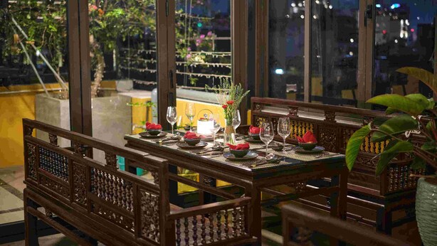 Un coin repas avec une table dressée pour quatre personnes, entourée de chaises en bois aux motifs complexes.