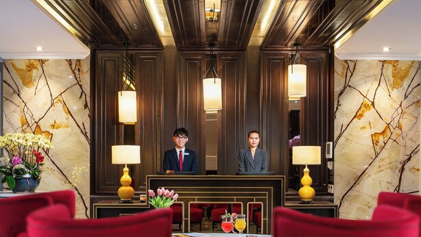 A hotel reception area with marble walls, red chairs, and a reception desk.