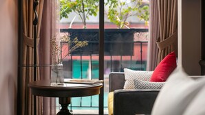 A cozy room with a table, a lamp, and a view of a balcony with plants and a railing.