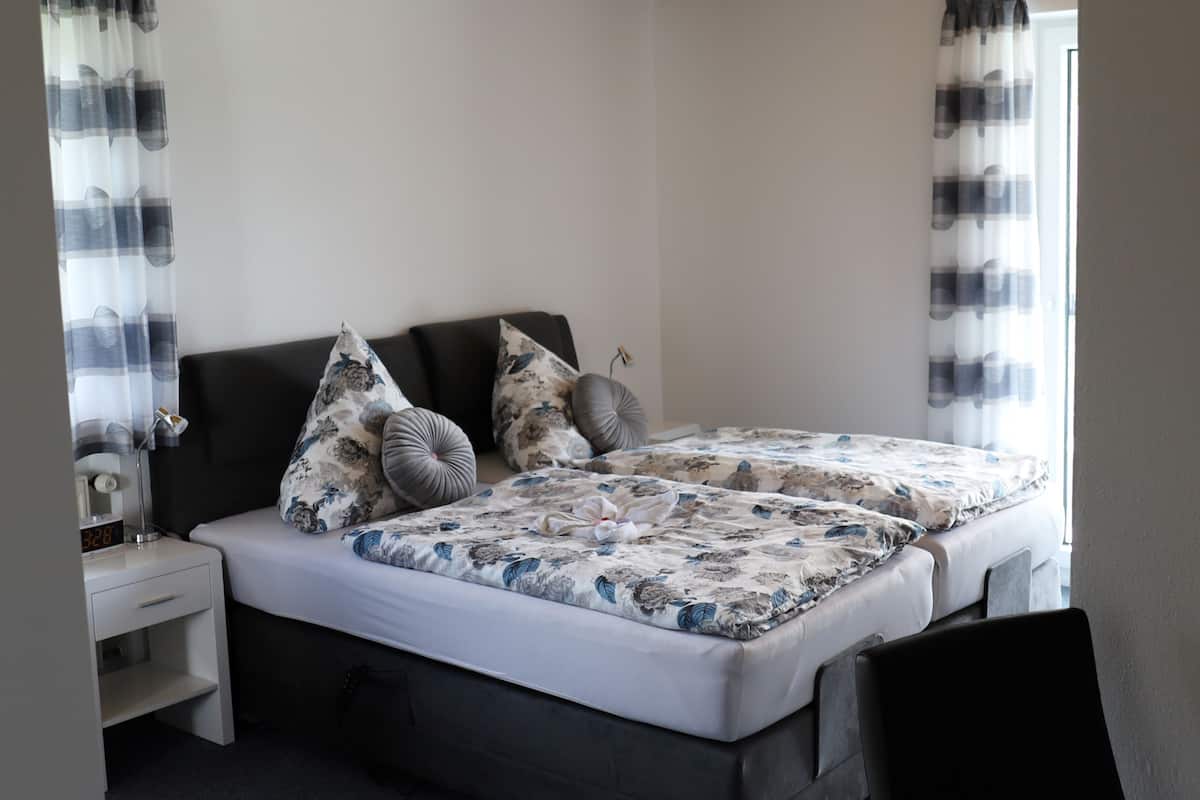 Una cama doble con ropa de cama floral, una mesita de noche con lámpara y un velador.
