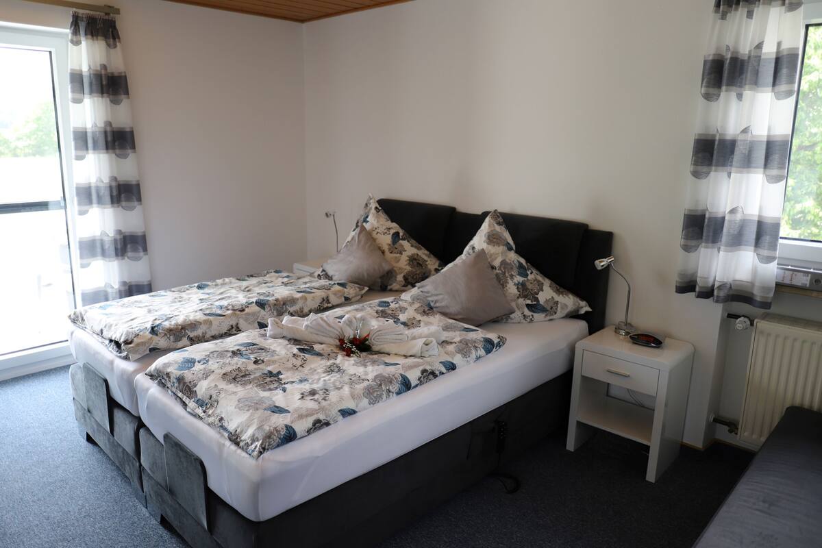 Un dormitorio con una cama doble, dos mesitas de noche, un radiador y una ventana con cortinas.